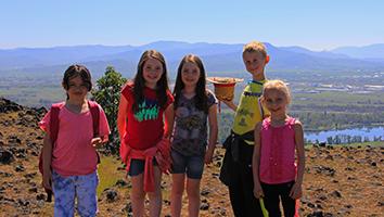 Five children stand smiling on top of a cliff.