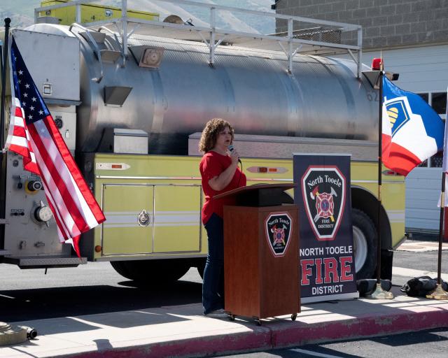 Rep. Celeste Maloy, R-UT speaks at the NTFD pushback ceremony. She stands at a podium and behind her is the water tender to be transferred as well as an American flag and a Utah state flag.