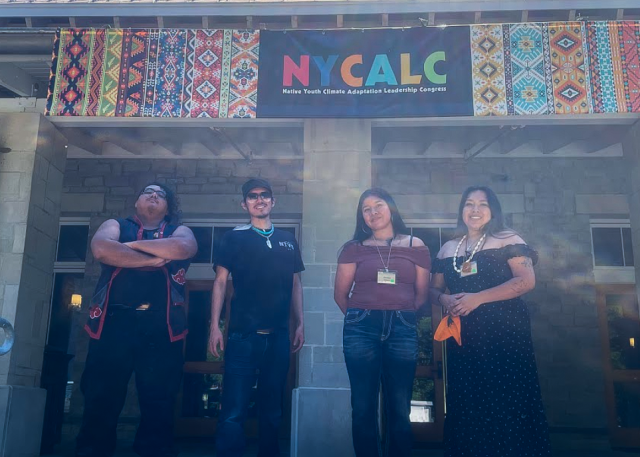 Four people stand together in front of a hanging poster.