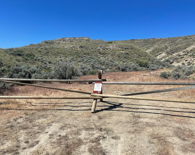 Bare ground with wooden fence and hills in the background.