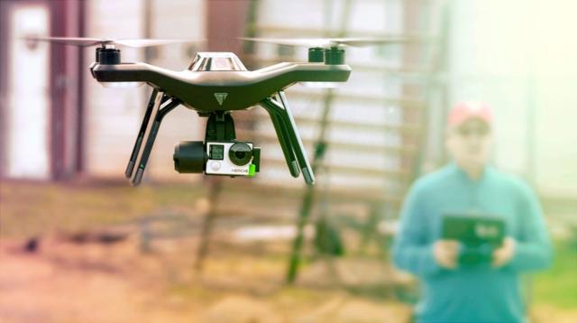 A small drone in the foreground with its operator out of focus in the background.