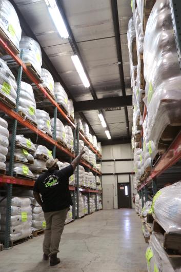 Person points up in the center of an aisle stacked to a high ceiling with large white bags