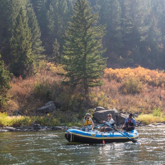 A photo of a raft on a river with fall foilage in the background.