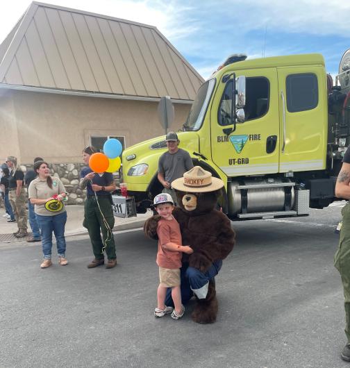 A young boy poses with Smokey Bear in front of a BLM fire truck