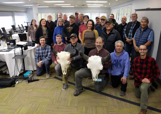 Group photo of the Lower Innoko and Yukon Rivers Wood Bison Planning Team meeting in Fairbanks, Alaska conference room. Two attendees hold two very large bison skulls in the front row.