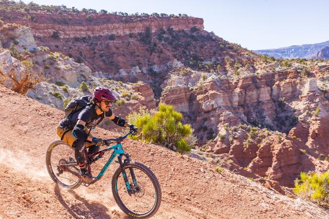 a mountain biker on a trail with red cliffs in the background