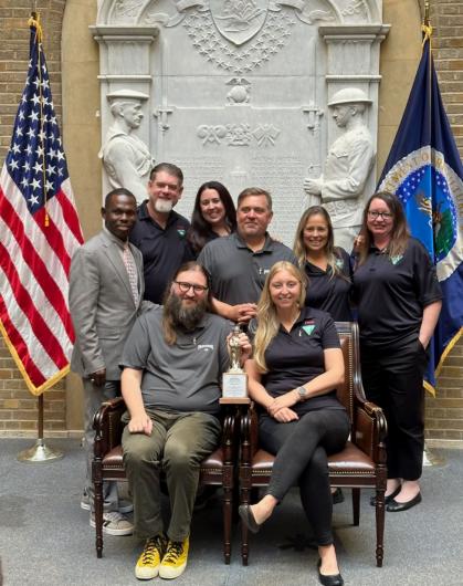 Group of people pose seated with American flag and trophy shaped like Smokey Bear