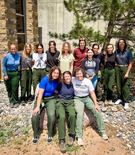 Female members of a fire crew encircle BLM Director standing outside next to a tree