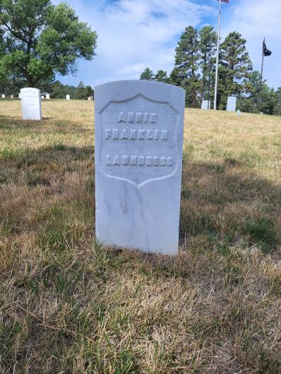 White gravestone on sunny hill with inscription that says Annie Franklin Laundress.