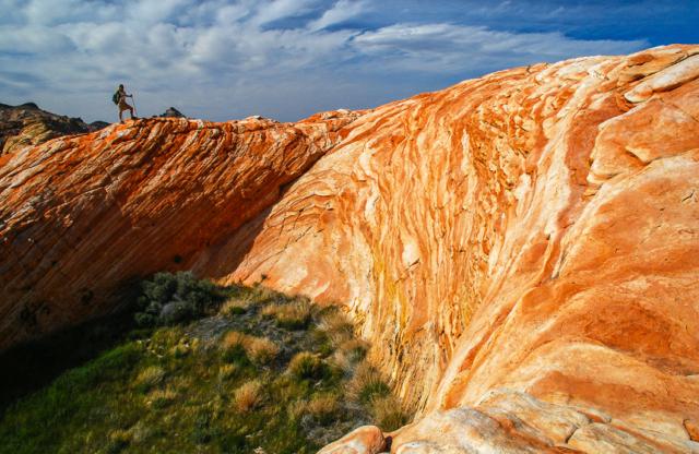 A hiker treks up the side of a rounded pattered sandstone formation