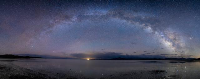 Night sky speckled with so many stars the arch of the Milky Way frames the horizon over water