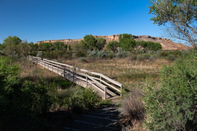 A bridge crosses a dry riverbed and a butte rises in the distance.