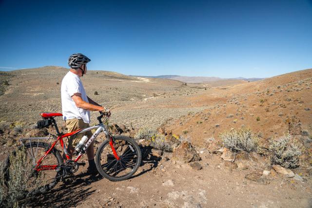 A man standing next to a bicycle overlooks a high desert landscape