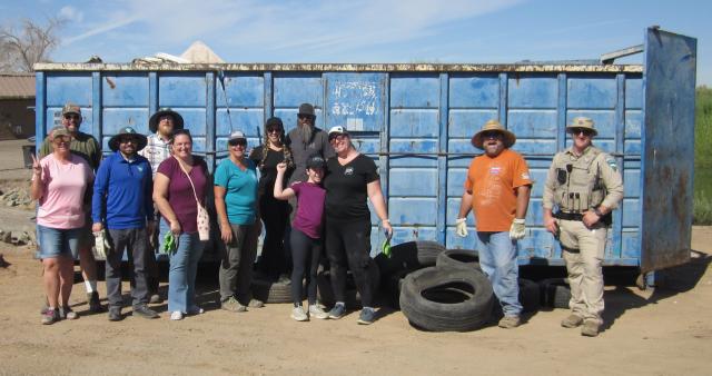 12 volunteers in front of a blue dumpster at the end of cleanup day.