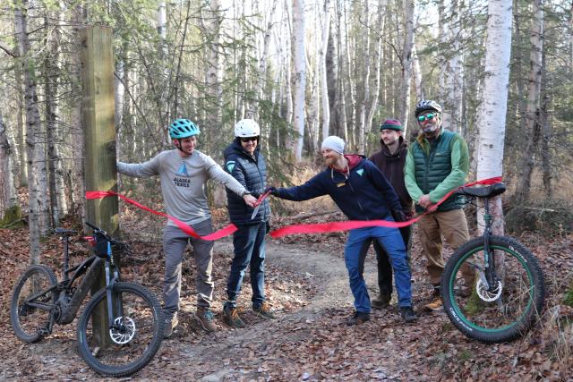 People with bikes cutting red ribbon.