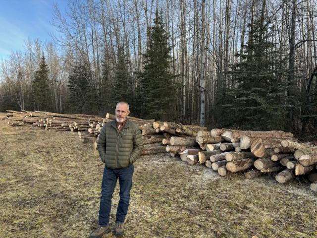 Caucasian man smiles in front of cut stacked logs 