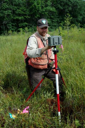 A man in BLM uniform operating a survey tool in a grassy field. 