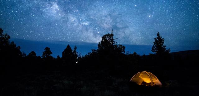 a lit up tent sits beneath a blanket of stars