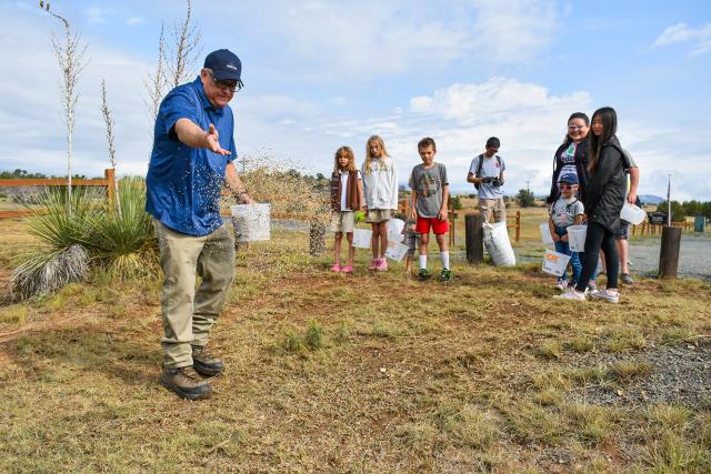 Michael McGee, left, a hydrologist in the Roswell Field Office, demonstrates how to distributes grass seed to volunteers.