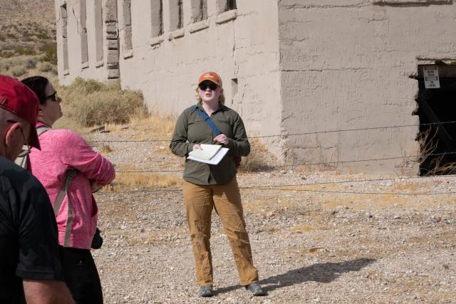 A person standing the foreground of an old building while talking to a group. 