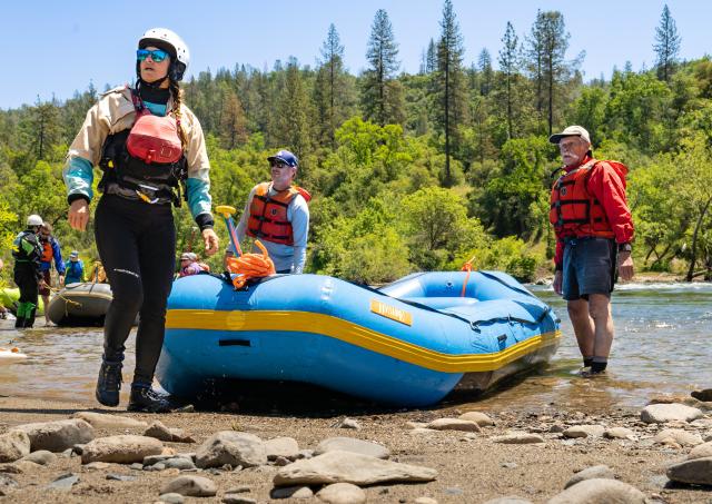 Rafters in whitewater gear exit a river in the forest.