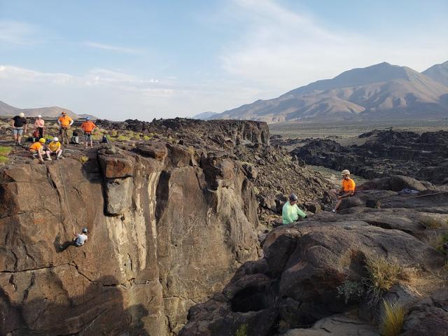 Rappelers descend a polished volcanic canyon. Large mountains in the background. 