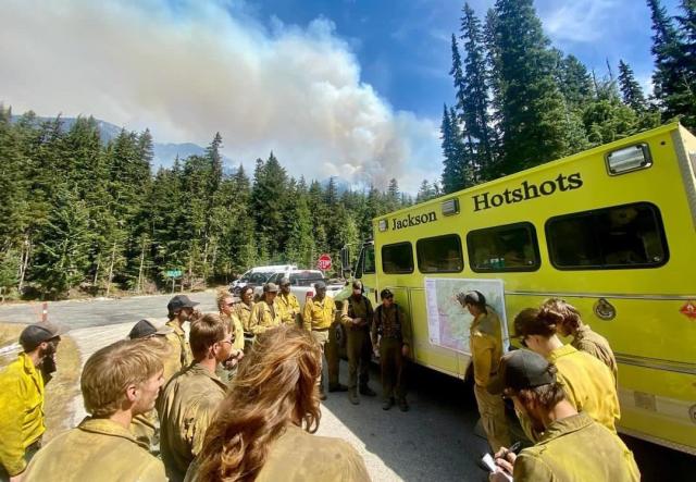 Jackson Hotshots firefighters gather around a truck, where one is pointing to a map attached to the side of the truck. 