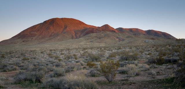 A large red mountain at sunset. Green and yellow brush in the foreground