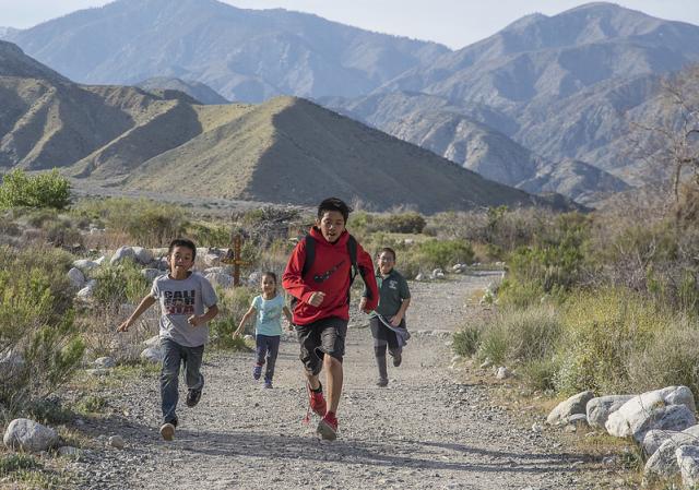 Children running on a desert path with larger mountains in the background.,