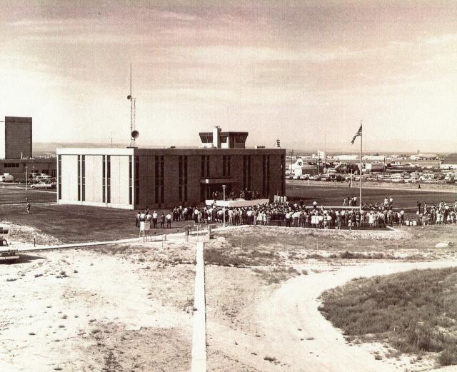 black and white image of a group of people standing outside of a rectangular building.