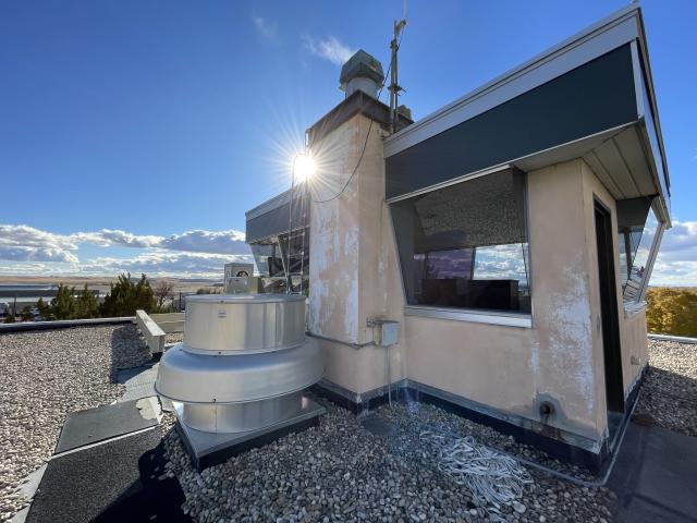 The sun shines from behind a small structure on a rooftop