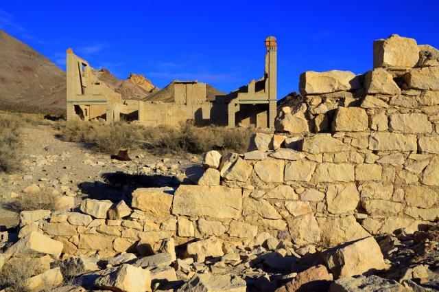 Remnants of a stone wall and in the desert distance, another partial building.