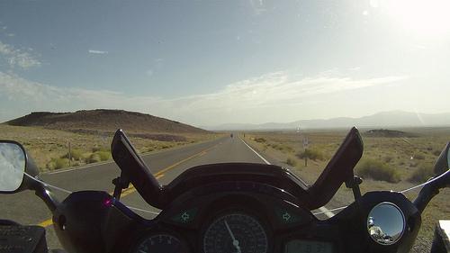 View of an open desert highway as seen behind motorcycle handlebars