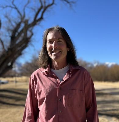 Neal Craig stands outside on a blue sky day with blurred tree in the background