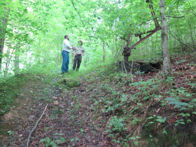 Two men stand on a path, an abandoned well is nearby to their right