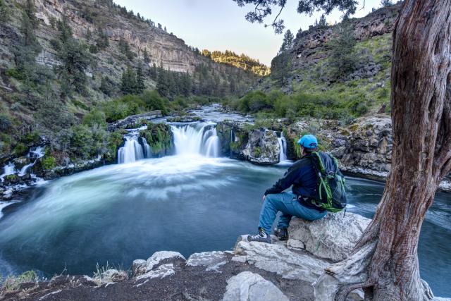 A man sits and looks at a waterfall at Arkansas River from the rocky edge of the river.