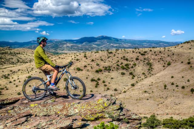 A mountain biker rests atop an outcropping, with the entire San Luis Valley laid out below.