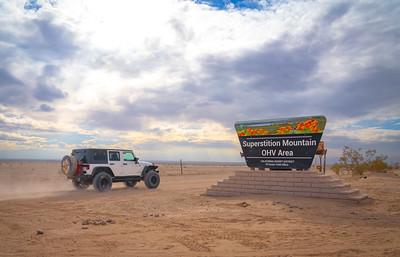 A white jeep drives by a sign reading, 'Superstition Mountains'