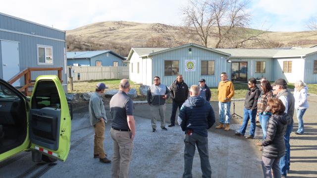 A circle of Native American and Caucasian people talk in a parking area.