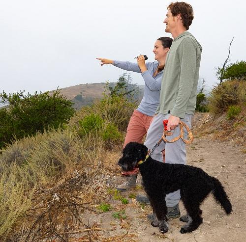 A woman, man, and dog look at something in the distance.