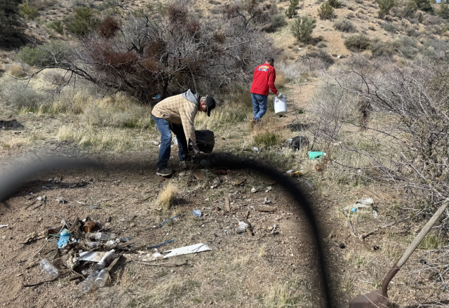 Two men cleanup a scattered trash pile in the desert.