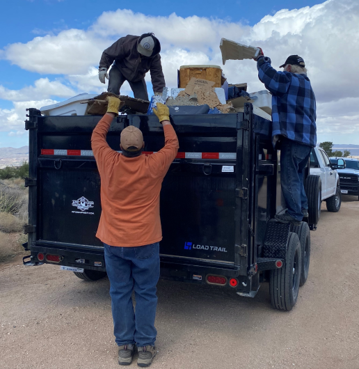 3 men load a trailer with trash for removal from the desert.