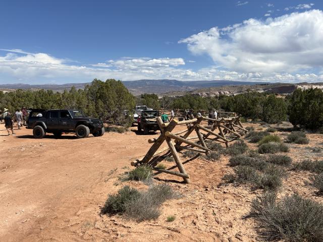 Buck-and-rail fencing, made entirely from wood posts, along a parking/staging area in the desert