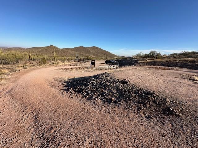 A photo showing a dirt path in a desert landscape that leads down a shallow slope to a small parking lot in the distance.