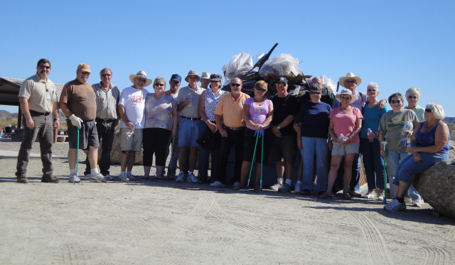 A group of volunteers pose in front of a dumpster full of garbage resulting from their cleanup efforts.