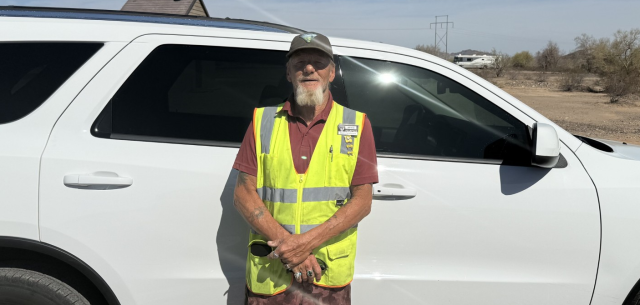 A volunteer man in a yellow safety vest poses in front of a white SUV.