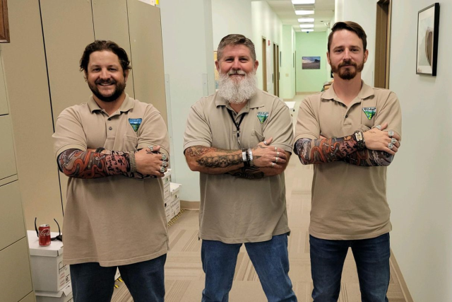 Three men pose together in an office hallway.