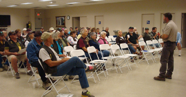 A man stands in front of a group of seated individuals in a training setting.