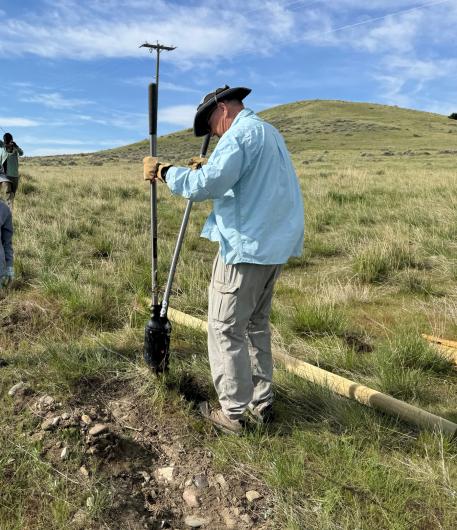 a person in a blue shirt digging a hole for a new fence post
