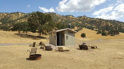 A dry campground with a vault toilet and a fire ring
